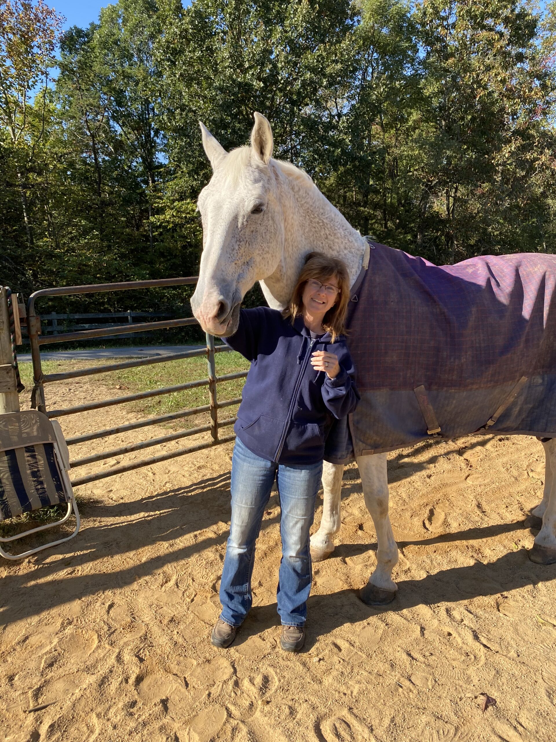 Susan Pyne, an employee at Stables Systems barn management software company, stands with a large gray horse. The horse is wearing a purple winter blanket